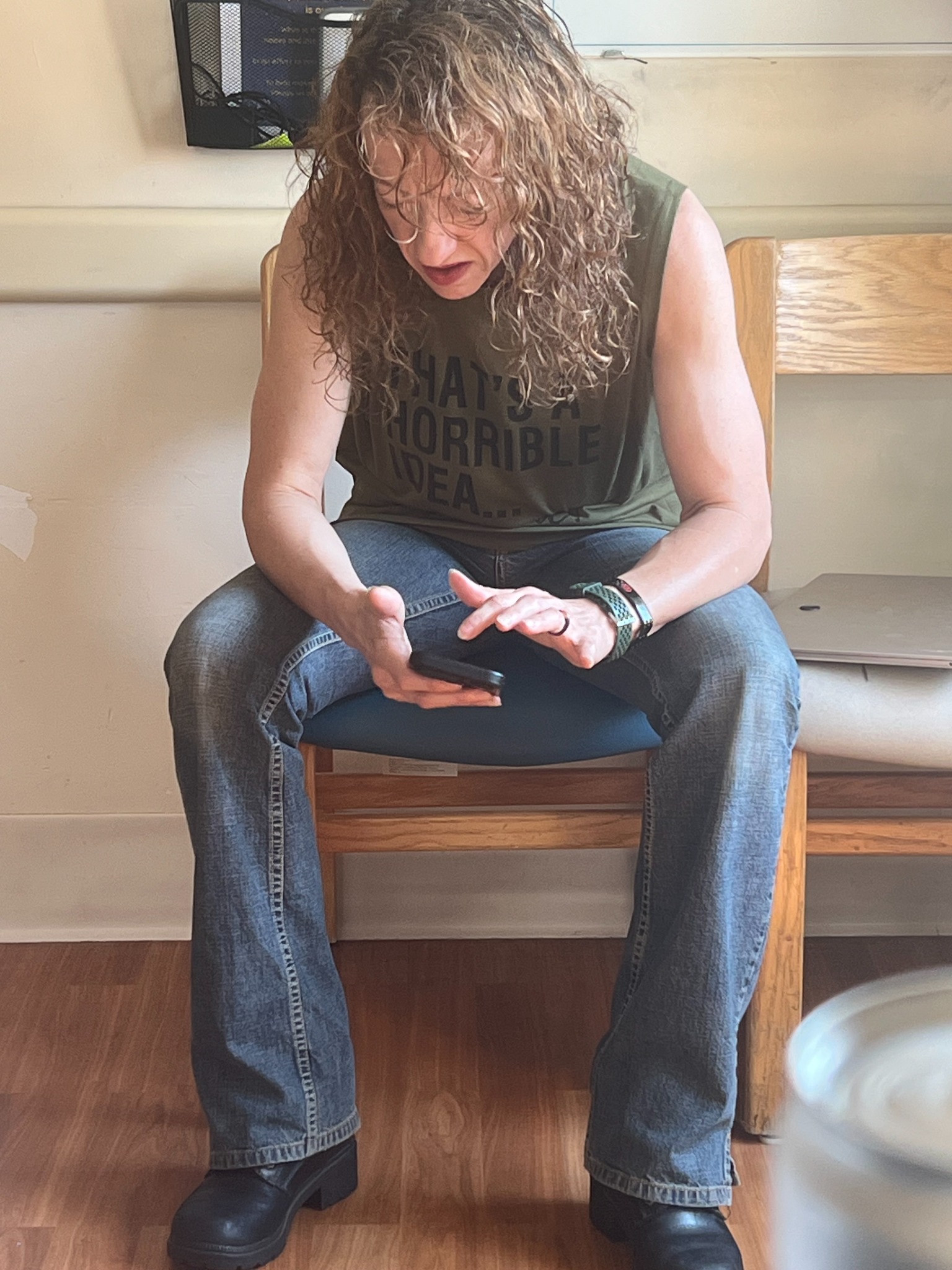 Christi Lynn seated in a green shirt, looking at her phone with a laptop beside her